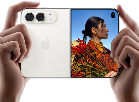 iPhone Duo, สีสตาร์ไวท์, ถืออยู่ในมือสองข้างในแนวนอน, กางเปิดอยู่, แผงด้านซ้ายแสดงกล้องหลัง Dual Fusion 48MP, แผงด้านขวาแสดงบุคคลหนึ่งขณะถ่ายภาพบนจอภาพภายนอก, ตัวแบบในภาพสามารถเห็นใบหน้าของตัวเองระหว่างกำลังถ่ายภาพโดยใช้ Duo Preview